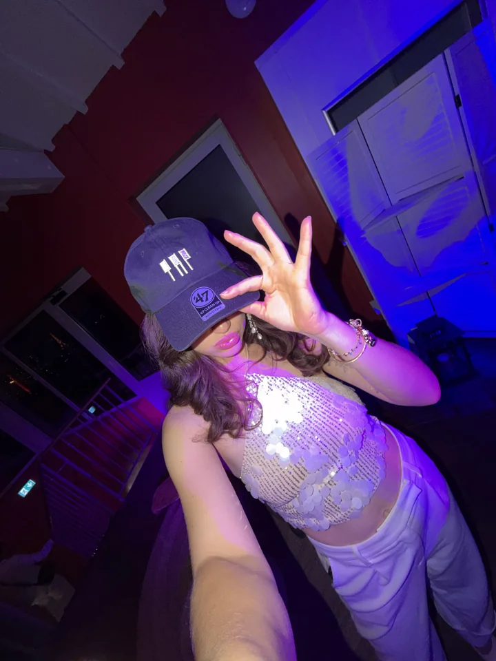 A woman wearing a TAP logo cap under purple lighting.